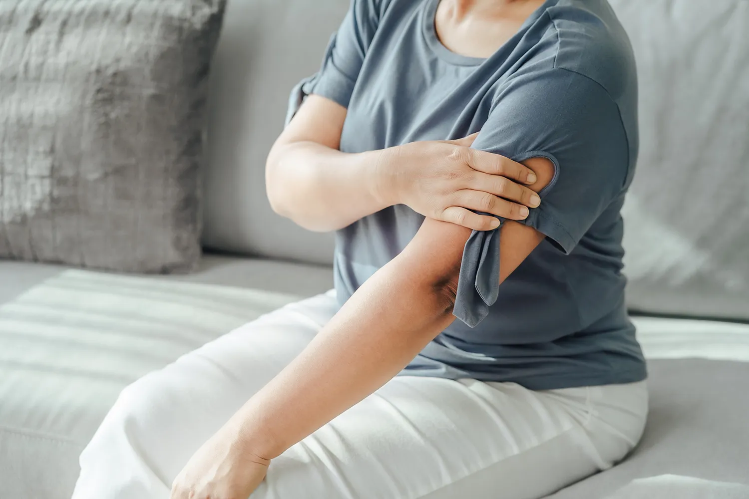 woman sitting in a couch holding her shoulder pain
