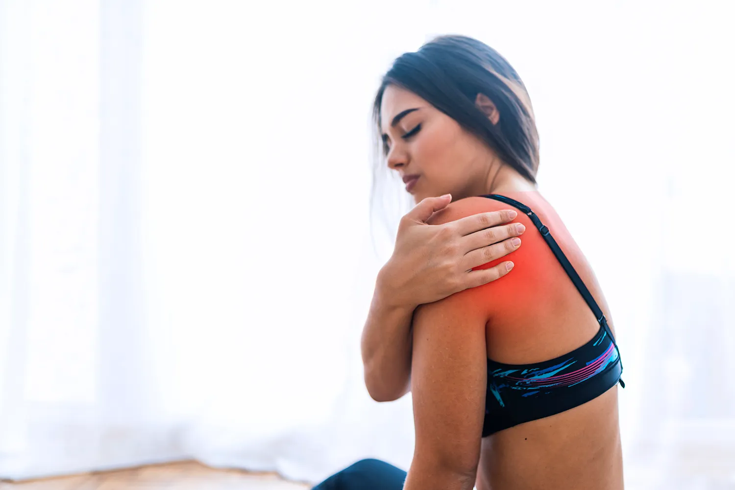 young woman sitting in a bed holding her shoulder due to pain